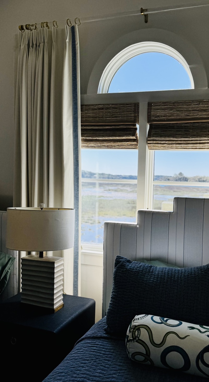 Custom pinch-pleat drapery with woven wood Roman shades in a coastal Charleston bedroom