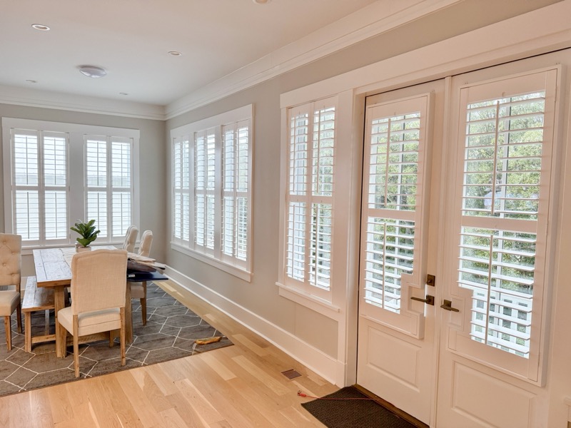 White plantation shutters spanning windows and French doors in a bright Charleston dining room